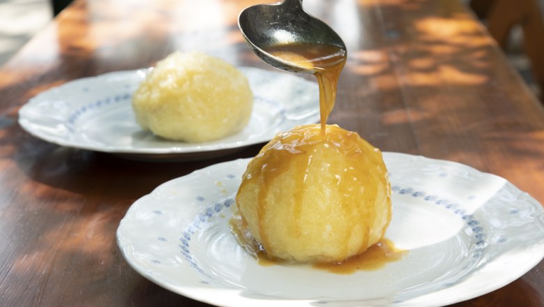 Knödelgericht, © Ben Leitner Ein Knödel auf einem Teller wird mit Soße übergossen, ein weiterer Knödel im Hintergrund.