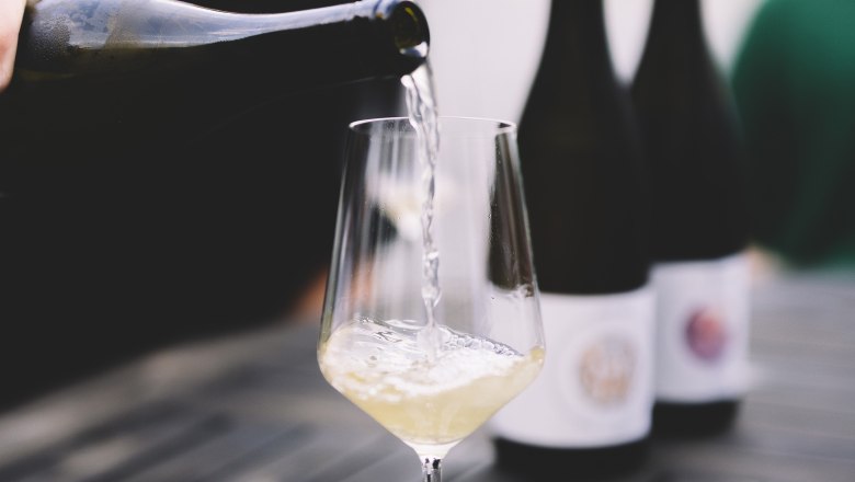 Wein einschenken, © Niederösterreich Werbung / Mara Hohla Weißwein wird in ein Glas auf einem Tisch eingeschenkt.