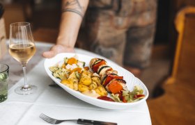 Ein Wirtshausklassiker: Grillspieß, © Niederösterreich Werbung/David Schreiber Ein Teller mit Grillspieß, Gemüse und Kartoffeln wird serviert, daneben ein Glas Weißwein.