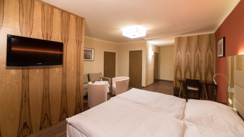Zimmeransicht, © Fam. Schweinberger Modern eingerichtetes Hotelzimmer mit Doppelbett, Fernseher, Sitzbereich und Holzmöbeln.