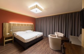 Zimmeransicht, © Fam. Schweinberger Modern eingerichtetes Hotelzimmer mit Doppelbett, Holzmöbeln und Vorhängen.