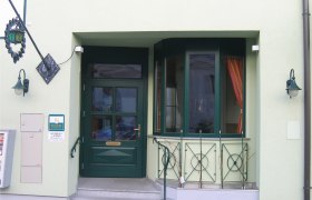 Eingangsbereich, © Fam. Laimer Eingangsbereich eines Gebäudes mit grüner Tür und Fenstern, dekoriert mit Pflanzen und Laternen.