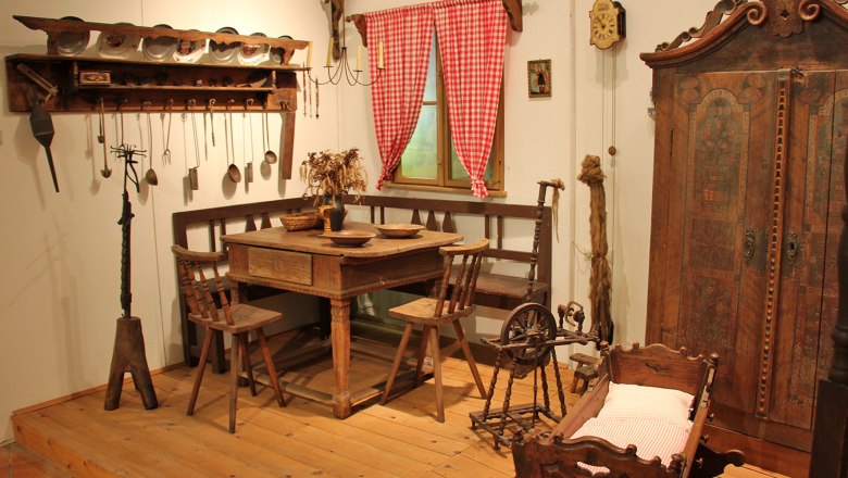 Historische Bauernstube mit Holzmöbeln, Spinnrad und Wiege.