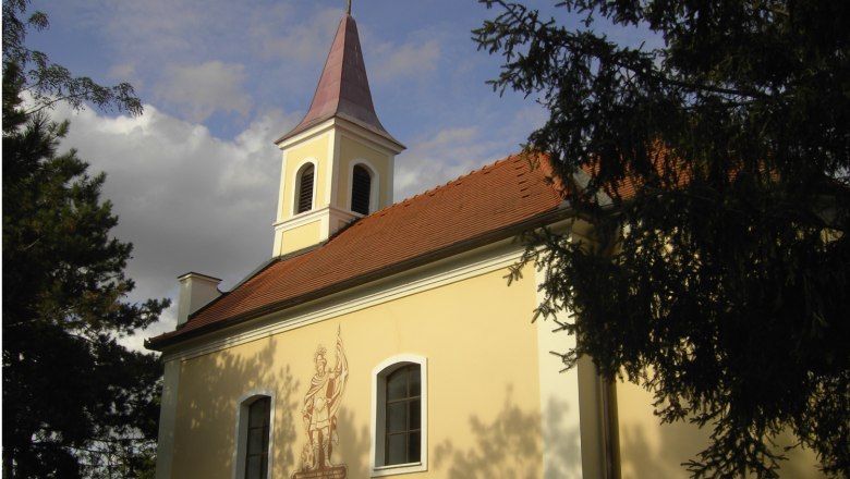 Florianikapelle Oberrohrbach mit Turm und Wandbild, umgeben von Bäumen.