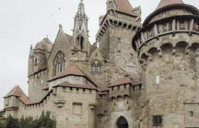 Zwei Personen stehen vor der Burg Kreuzenstein, umgeben von alten Steinmauern und Türmen.