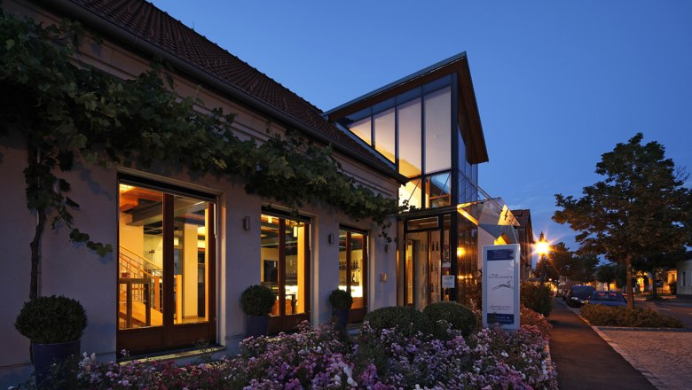 Abendaufnahme eines modernen Gebäudes mit Glasfassade und Blumenbeeten.