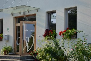 Wein + Bett Wiedeck, © Andrea Wiedeck Eingang eines Gebäudes mit der Aufschrift 'wein + bett', umgeben von Blumen.