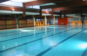 Innenansicht eines Schwimmbads mit leeren Liegest&uuml;hlen am Beckenrand.