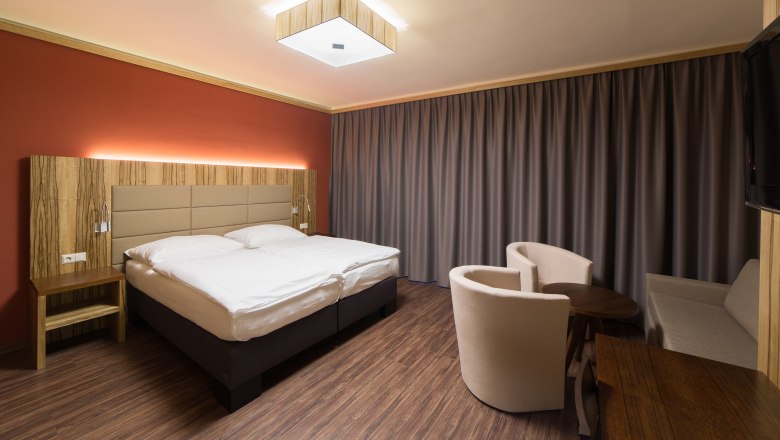Zimmeransicht, © Fam. Schweinberger Modern eingerichtetes Hotelzimmer mit Doppelbett, Holzmöbeln und Vorhängen.