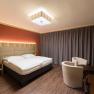 Modern eingerichtetes Hotelzimmer mit Doppelbett, Holzmöbeln und Vorhängen.