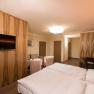 Modern eingerichtetes Hotelzimmer mit Doppelbett, Fernseher, Sitzbereich und Holzmöbeln.