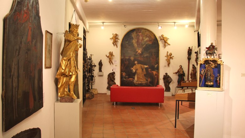 Innenansicht eines Museums mit Skulpturen und Gem&auml;lden, rotes Sofa in der Mitte.