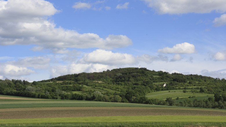 Landschaft mit H&uuml;geln und Feldern unter blauem Himmel mit Wolken.