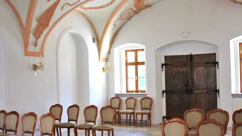 Innenansicht eines historischen Raumes mit verzierten Stuckdecken und eleganten Holzstühlen.