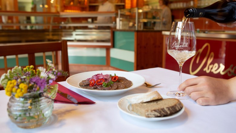 Ein gedeckter Tisch in einem Heurigenlokal mit einem Teller Essen, Brot und einem Glas Wein.