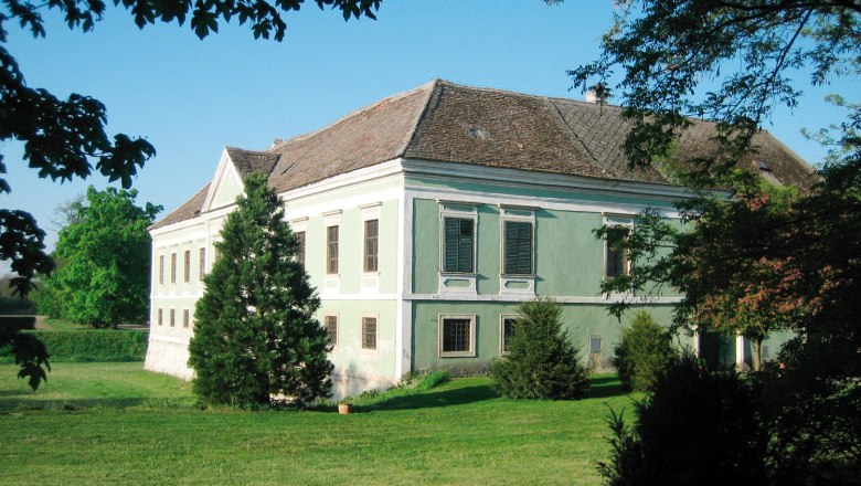 Ein altes Schloss mit gr&uuml;nem Anstrich und Ziegeldach, umgeben von B&auml;umen und Rasen.